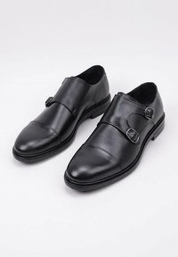 Zapatos de cuero negro con un diseño de punta redondeada, que cuentan con acentos de doble hebilla y una textura suave. Ligeros con un tacón bajo.
