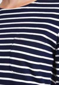 Marinblå och vit randig långärmad skjorta med rund halsringning och ficka på vänster sida, tillverkad av mjukt, texturerat tyg.