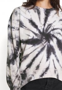 Sudadera de manga larga en tonos gris y negro con efecto tie-dye, que presenta un dobladillo curvado y un diseño floral adornado con cuentas.