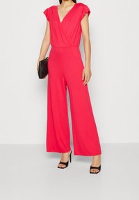Raspberry pink jumpsuit with a deep V-neck and flared wide legs. Features pleated short sleeves and a smooth fabric texture.