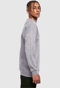 Šedá mikina s dlouhými rukávy vyrobená z měkkého materiálu. Má vroubkovaný výstřih a manžety a rovný lem. Jednoduchý, minimalistický design.