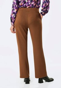 Donkere flared pants gemaakt van zachte stof, met een gladde textuur en een hoge taille. Draagt een kleurrijke blouse met patroon en zwarte hakken.