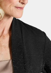 Zwarte glinsterende jas met een zachte textuur en een open voorkant. Beschikt over een lichtgewicht stof en subtiele glans overal.