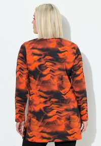Long-sleeve tunic in orange and black abstract print. Features a rounded hem and side slits for added movement. Soft fabric texture.