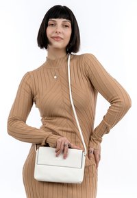 Bolso cruzado de cuero blanco con un diseño minimalista, que presenta una solapa plegable y una fina correa ajustable. Vestido de punto acanalado texturizado en beige.