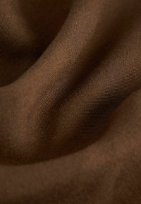 Tissu brun avec une texture douce, affichant de fins détails de tissage et des ondulations légères, indicatifs de douceur et de fluidité.