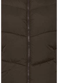 Gros plan d’un tissu matelassé brun foncé avec une fermeture éclair métallique centrée, verticale.
