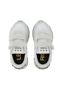 Scarpe da ginnastica bianche con un design a strappo in velcro, materiale sintetico liscio, punta arrotondata e un accento nero sulla suola con scritte gialle.