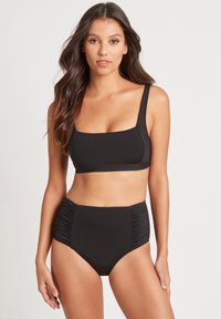 Zwarte tweedelige badpak met een rechthoekig topje met brede schouderbanden en hoge taille broekjes met geplooide zijkanten. Soepele textuur.