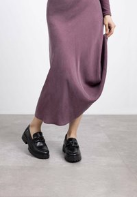 Mocasines negros con suelas gruesas, un detalle de cadena en la parte frontal, combinados con un vestido largo y fluido de color púrpura en una tela suave. Textura lisa.