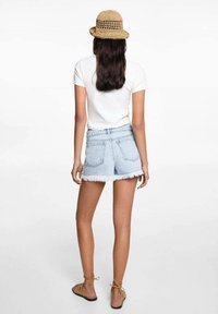 Svijetloplave traper šortse s izbrušenim rubom, uparene s bijelom majicom i slamnatim šeširom. Sandale s vezicama oko gležnja upotpunjuju outfitu.