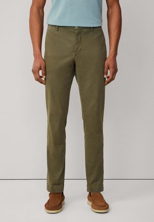 Pantaloni in cotone verde oliva con taglio slim, dotati di zip, passanti per cintura e orli arrotolati, abbinati a scarpe slip-on in suede marroni.