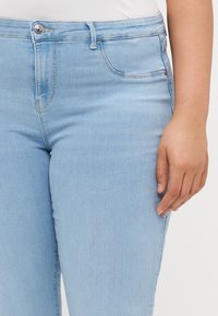 Light blue denim jeans with a smooth texture, five-pocket design, and a button closure. Features a straight leg cut and minimal stitching details.