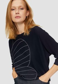 Czarny top z długim rękawem z białym liniowym wzorem liści z przodu. Miękka tekstura, luźny krój i okrągły dekolt.