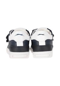 Un paio di sneakers bianche e nere viste da dietro, con un logo a silhouette di gatto nero sulla linguetta bianca del tallone.