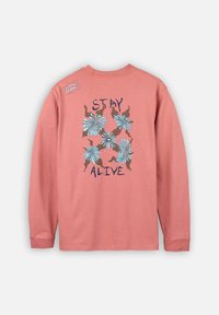 Chemise en coton à manches longues, de couleur rose corail avec un motif floral bleu. Texte "RÉSISTER" imprimé en gras noir. Étiquette sur l'épaule.