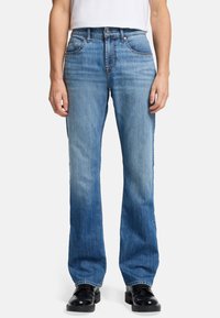 Un jean en denim bleu clair présente une coupe droite, dégradé de clair à foncé, avec deux poches avant et une fermeture éclair.