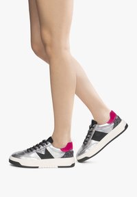 Scarpe da ginnastica argento con dettagli neri e tacco in suede rosa. Presentano una parte posteriore testurizzata e una suola nera testurizzata. I lacci sono neri.