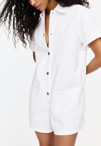 Witte denim playsuit met korte mouwen, een knoopsluiting aan de voorkant, twee grote voorzakken en een kraag. Glad textuur, casual ontwerp.