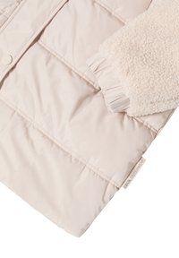 Veste matelassée rose clair avec un design matelassé, poignets en polaire crème texturée, détail de poignet froncé et étiquette du fabricant sur l'ourlet.