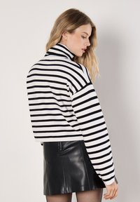 Schwarz-weiß gestreifter Rollkragenpullover mit langen Ärmeln, gerippten Bündchen und cropped Länge, kombiniert mit einem schwarzen Lederrock.