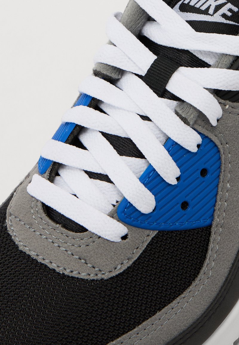 Sneakers Nike z czarną siateczką i szaro-zamszowym wierzchem, z białymi sznurowadłami i niebieskim akcentem po boku. Teksturowany design z przeszyciami.