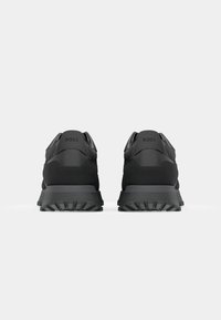 Paire de baskets noires BOSS vues de dos, montrant des semelles texturées et un marquage sur les languettes de talon sur un fond uni.