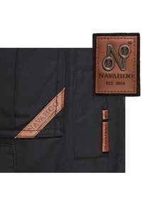 Tessuto nero con toppe in pelle. Le toppe presentano il logo "Navahoo" e "EST 2014" in argento e marrone. Dettaglio cucito vicino alla tasca.