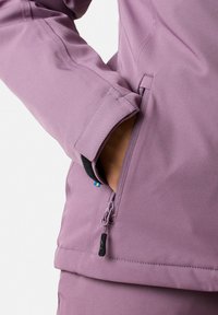 Lila softshell-jacka med dragkedjeförsedda sidfickor och kontrasterande innerfoder vid ärmslutet. Har en slät textur och en skräddarsydd passform.