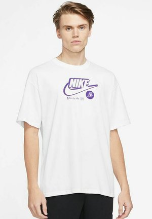 T-shirt in cotone bianco con un grande logo Nike viola e stampa grafica. Maniche corte, vestibilità rilassata e collo a giro.