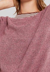 Trui van zachte roze gebreide stof met een gestructureerd patroon. Het heeft een ronde halslijn en een gestreepte bruingrijze en witte kraagdetail.