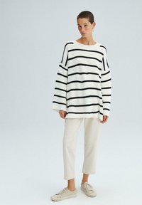 Pull en tricot blanc avec des rayures horizontales noires, manches larges, encolure ronde ; assorti à un pantalon clair et des baskets.