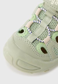 Πράσινο αθλητικό παπούτσι από δίχτυ με λαστιχένια σόλα, ελαστικά κορδόνια, μπεζ λεπτομέρειες και οπές αερισμού για καλύτερη αναπνοή.