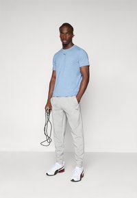 Lyseblå trenings-T-skjorte, grå joggebukser og hvite sneakers med røde detaljer. Personen holder et hoppetau.