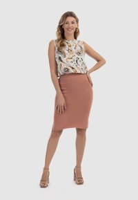Bezramenný top s květinovým vzorem v kombinaci s přiléhavou sukní po kolena v jemné růžové barvě. Modelka stojí sebevědomě a má na sobě béžové sandály na kostkách.