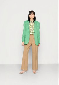Blazer verde, blusa floral, calças largas bege e sandálias claras. Texturas suaves; design ajustado com ombros estruturados.