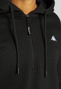 Sudadera con cremallera negra hecha de tejido suave, con un pequeño logo blanco en el pecho, cordones y una cremallera lisa.