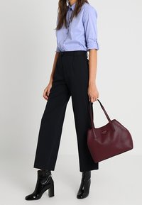 Lichtblauw overhemd met knopen, zwarte broek met wijde pijpen, zwarte enkellaarzen met glanzende afwerking, en een bordeauxrode handtas met een gestructureerd oppervlak.