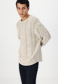 Ανοιχτό μπεζ πλεκτό πουλόβερ με υφή καλωδίου, διαθέτει στρογγυλή λαιμόκοψη και φαρδιές κοντές manches.