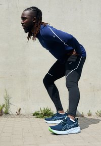 Calzature sportive in blu navy e verde lime, abbinate a leggings neri e a una maglia a maniche lunghe blu con dettagli riflettenti.