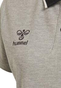 Grå polo tröja med en texturerad tyg. Har en broderad bi-logga och ordet "hummel" i mörk tråd på vänster sida.