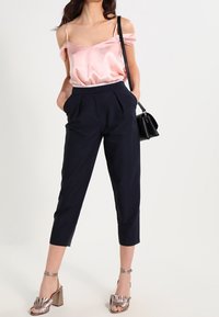 Off-the-shoulder satin rosa topp, högmidjade marinblå byxor och metalliska remsandaler med klossklack, tillsammans med en liten svart handväska.