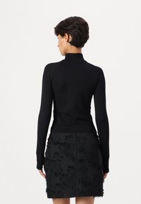 Black long-sleeve turtleneck top paired with a fitted black skirt featuring textured, layered fringes. Smooth, stretchy fabric.