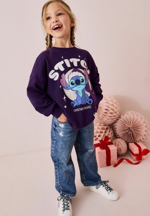 Lila Sweatshirt mit einem "Stitch"-Grafikdesign und Glitzerakzenten, kombiniert mit hellblauen, zerrissenen Jeans und weißen Sneakern.