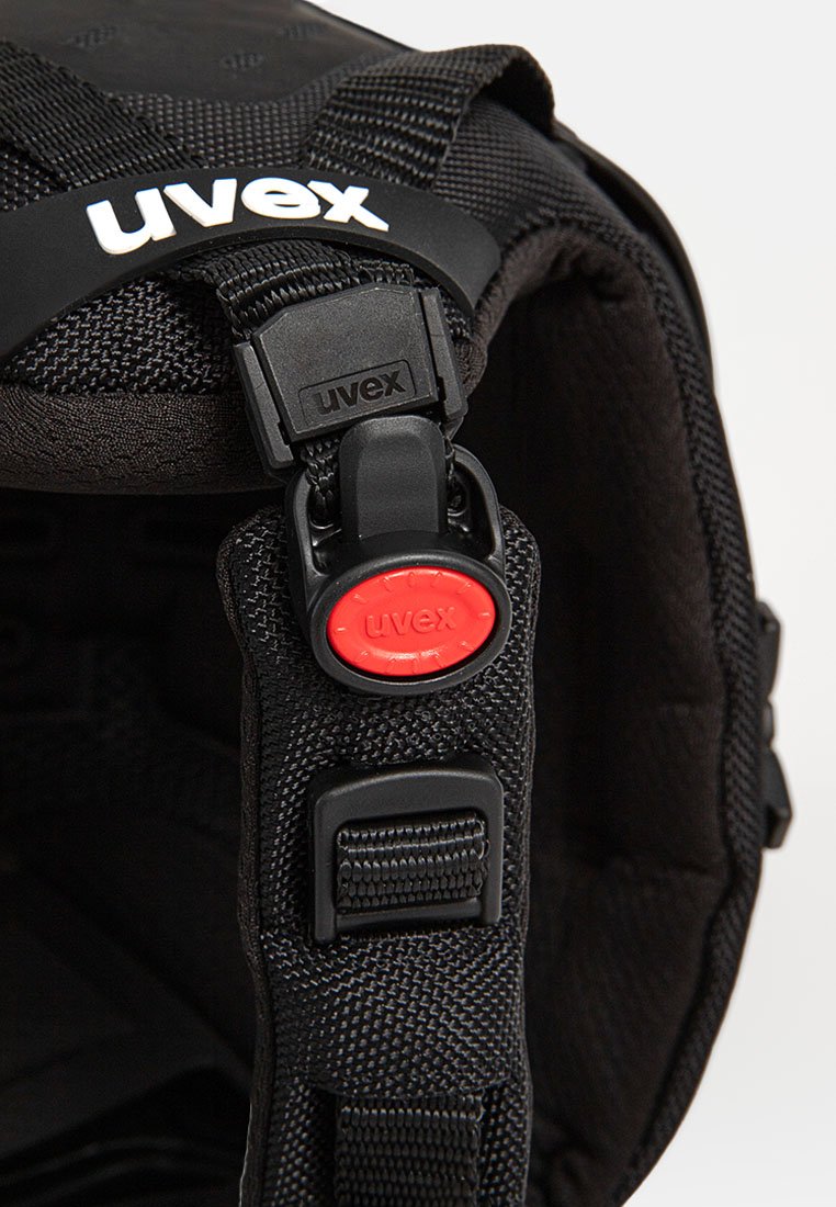 Schwarzer Helm mit strukturiertem Stoff, verstellbaren Riemen und einem auffälligen roten Auslöser. Mit dem "uvex"-Logo auf einem schwarzen Riemen.
