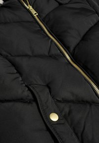 Schwarze Pufferjacke mit einem gesteppten Design, ausgestattet mit einem goldenen Reißverschluss und Druckknopfverschluss. Das Material hat eine glatte, matte Textur.