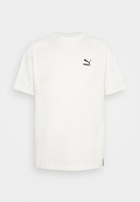 Bílá bavlněná tričko s kulatým výstřihem a krátkými rukávy. Na hrudi se nachází černé logo Puma a na boku je malá štítek s logem.