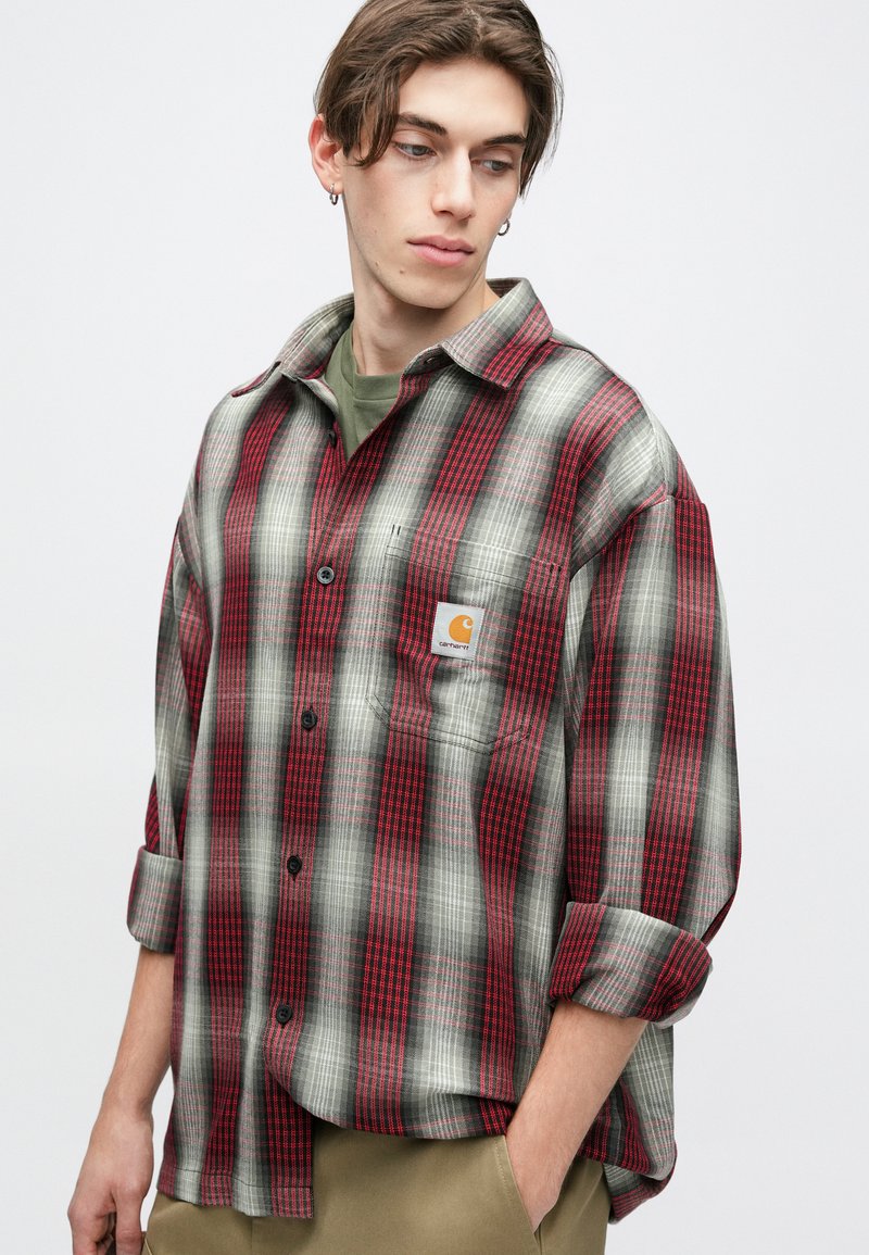 Red and gray plaid flannel shirt with a relaxed fit, single chest pocket, and logo patch. Features button closure and rolled sleeves.