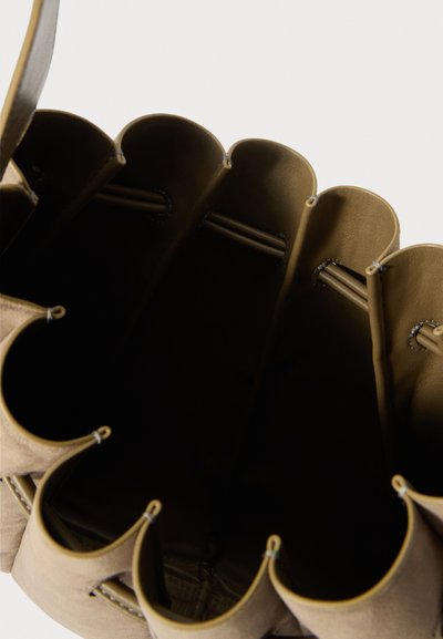 Otevřená hnědá kožená kabela ve tvaru kbelíku, která má vykrajované okraje a viditelné stehy na vnitřní podšívce, na bílém pozadí.