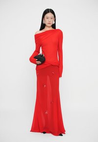 Piros, vállat szabadon hagyó ruha hosszú ujjakkal, tágas szoknyával és virágos díszítésekkel. A model fekete clutch táskát tart. Simább, könnyű anyag.